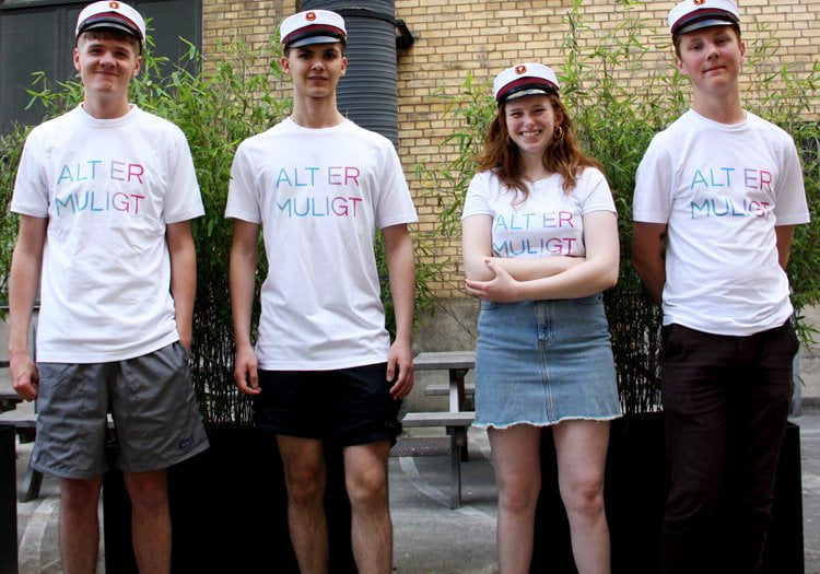 Fire nybagte studenter med studenterhuer på og en t-shirt med teksten: Alt er muligt