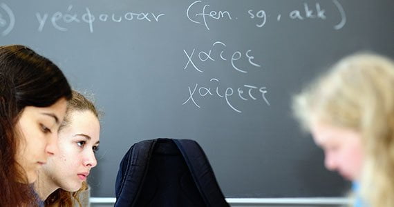 Elever i profil med tavle i baggrunden, hvor der er skrevet ord på græsk