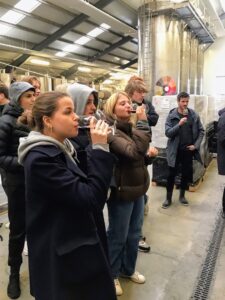 En gruppe elever smager på kirsebærvin i en stor hal til vinproduktion