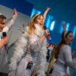 Elever spiller musicalen Mamma Mia. Piger klædt i hvidt tøj synger på en scene.