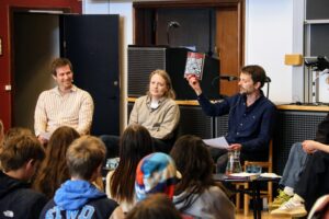 Forfatter og psykolog Glenn Bech på Gefion Gymnasium. Sidder ved et bord sammen med to lærere og to elever foran et publikum af elever. I Festsalen på Gefion. Den ese lærer holder Glenn Bechs bog "Jeg anerkender ikke længere jeres autoritet" op foran publikum.