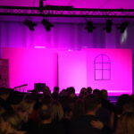 Gefions elevproducerede musical 2024: Mean Girls. Scene med lyserød baggrund. Publikum ses bagfra, sidder i mørket.