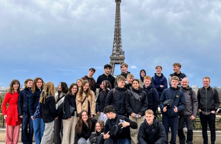 En klasse står foran Eiffeltårnet i Paris på studietur.