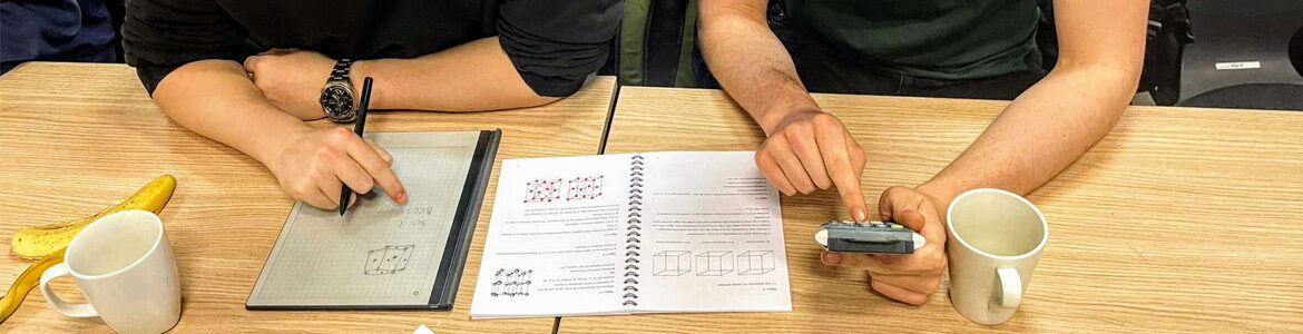 Et sæt hænder arbejder med lommeregner og blyant ved et bord med matematikpapirer, krus og en banen