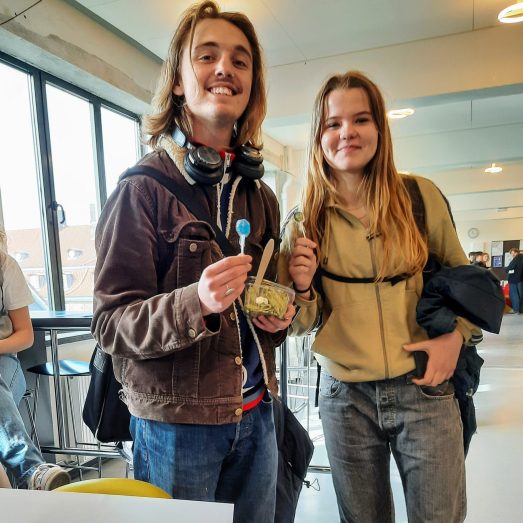 En dreng og en pige smiler til kameraet og holder hver deres slikkepind i hånden
