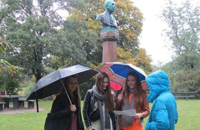 Elever med paraply foran buste i park i regnvejr