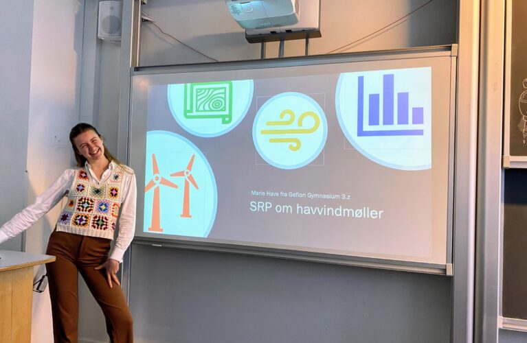 Gefion Science Fair 2023. En pige foran tavle med forsiden af sit SRP-projekt om havvindmøller.