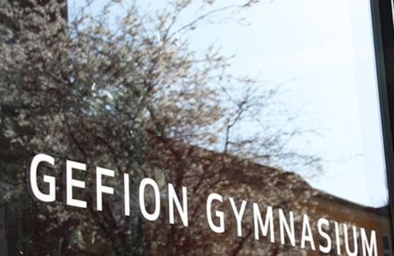 Glasdør ved indgangen til Gefion Gymnasium hvor blomstrende træer spejler sig i ruden