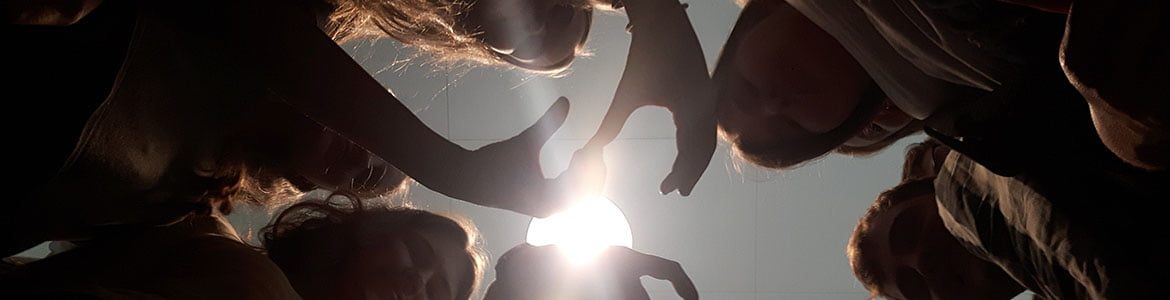 Elever i silhouet der laver tegn med hænderne set nedefra mod solen